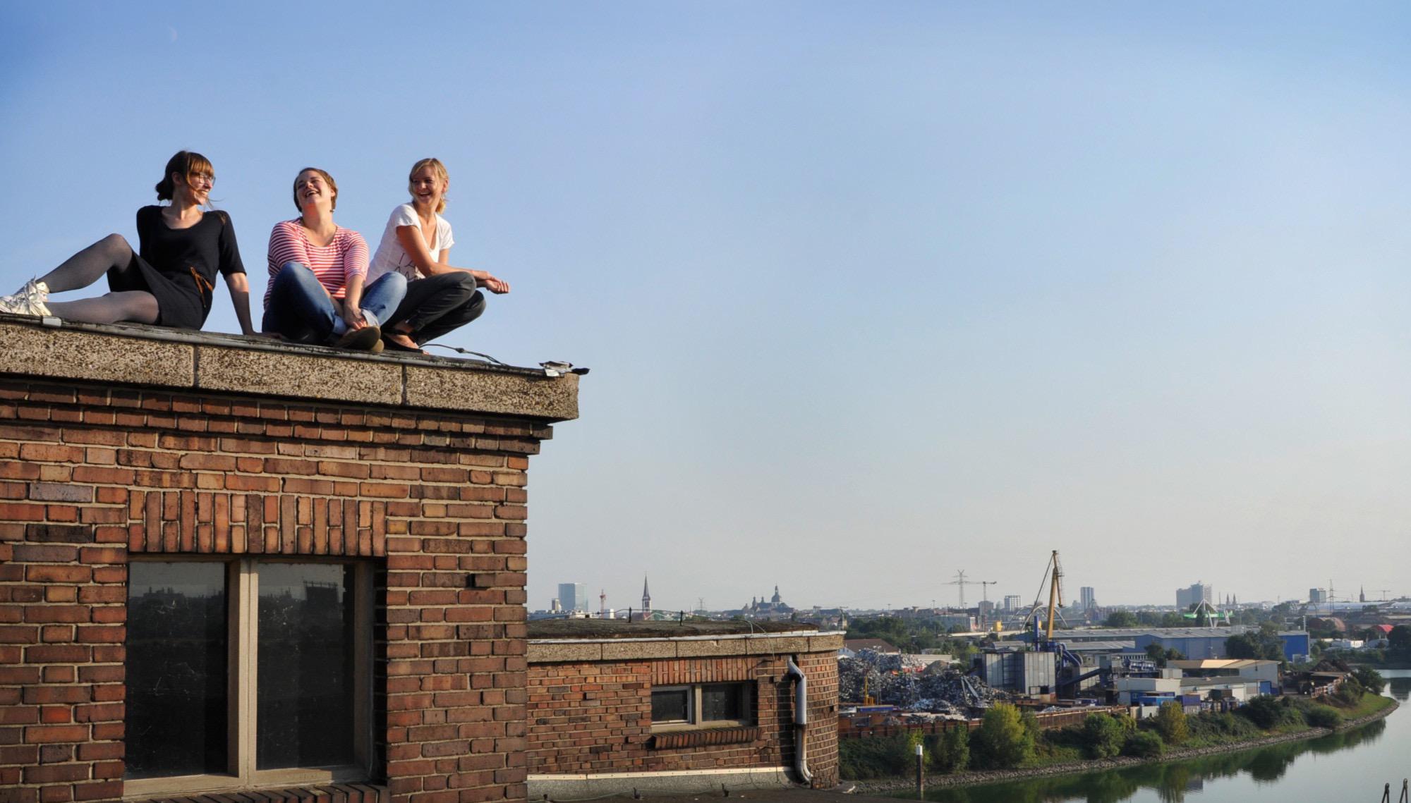 Die Gründerinnen Annika Wind, Anne Jeschke und Sarah Weik sitzen auf einem Dach über der Stadt.